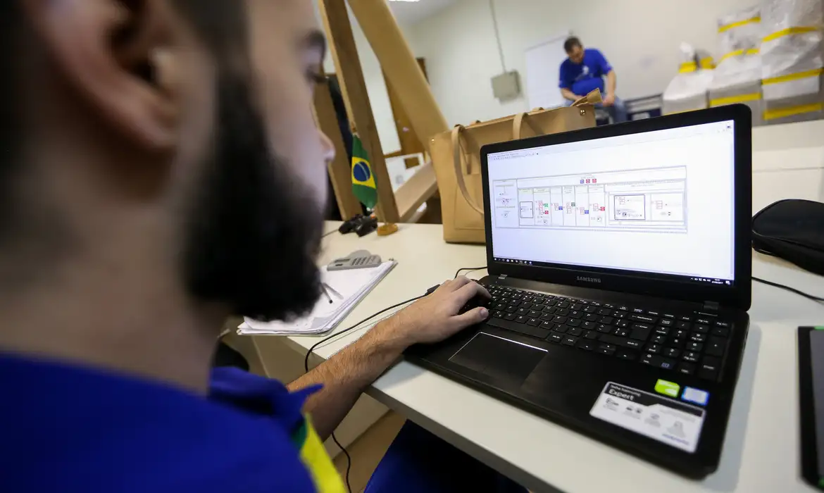 Profissional analisando dados em notebook Samsung Homem de camiseta azul olhando para tela de notebook Samsung com gráficos e diagramas na mesa de escritório.