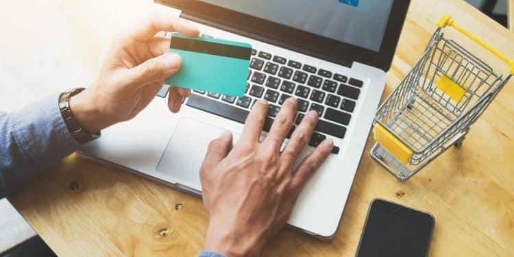 Pessoa segurando cartão de crédito e digitando no notebook para compra pela internet.
