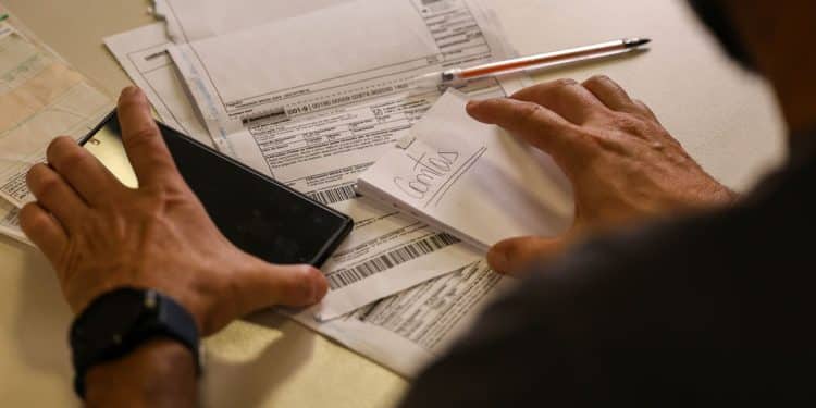 Pessoa organizando boletos bancários e documentos financeiros sobre mesa