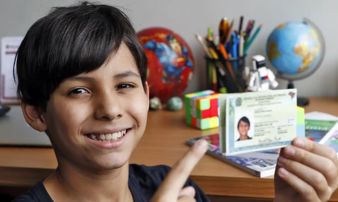 Como funciona o atendimento especial neste sábado. Criança sorridente mostrando sua nova Carteira de Identidade Nacional emitida em atendimento especial do SAC.