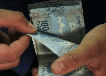 Duas mãos contando cédulas de cem reais referente ao pagamento da segunda parcela do décimo terceiro.