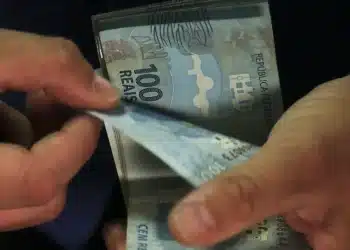 Mãos manuseando cédulas de cem reais representando suposta premiação por nota alta no Enem.