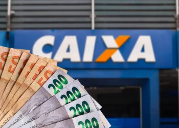 Notas de R$ 50 e R$ 200 em primeiro plano, com a fachada da agência da Caixa Econômica Federal ao fundo, representando o pagamento de R$ 2.800.