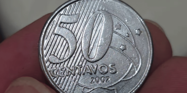 Close-up ampliado da moeda de 50 centavos do ano de 2002, em foco nos números e na palavra "CENTAVOS". A imagem destaca a busca por erros raros de cunhagem que podem elevar seu valor para colecionadores até R$ 400.