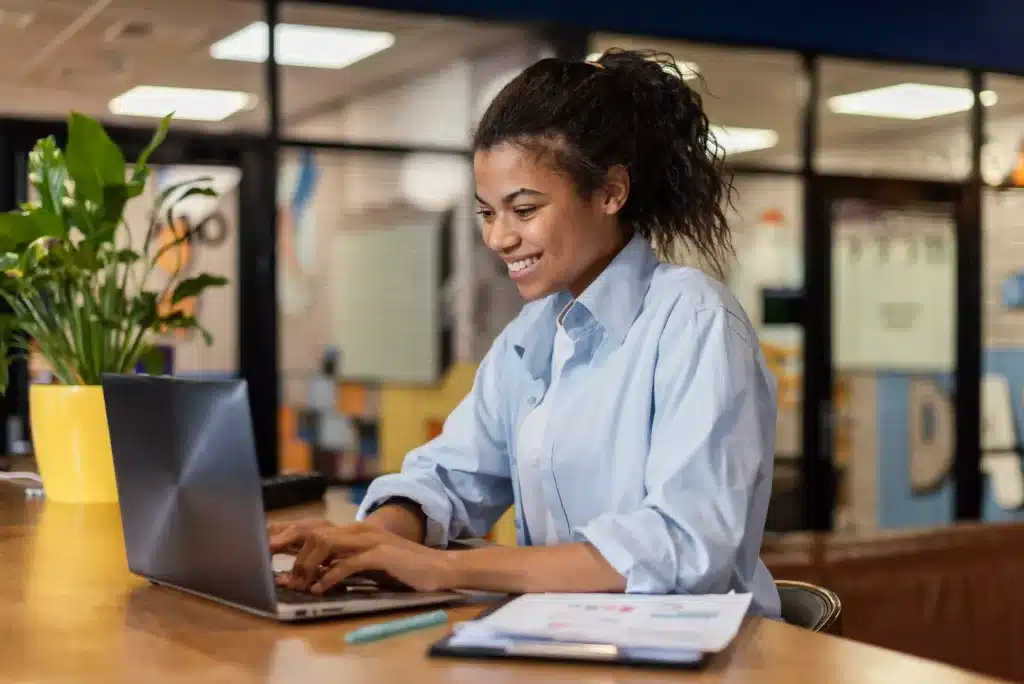Como se preparar para conquistar um bom salario Mulher sorridente trabalhando no computador em um escritório.