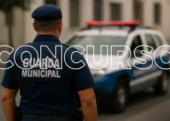 Guarda Municipal de costas usando uniforme azul com viatura policial ao fundo