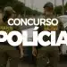 Dois policiais militares de costas em uma rua, ao lado de viatura oficial da polícia.