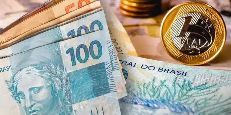 Composição com notas de 100 e 50 reais em primeiro plano, moedas empilhadas ao fundo e uma moeda de 1 real em destaque à direita.