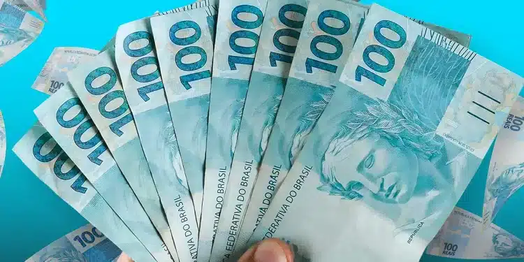 Mão segurando várias cédulas de 100 reais brasileiras com notas de 100 reais voando ao fundo azul