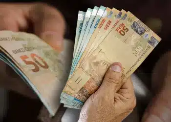 Mãos segurando e contando várias notas de dinheiro em reais, com destaque para cédulas de 50 e 2 reais