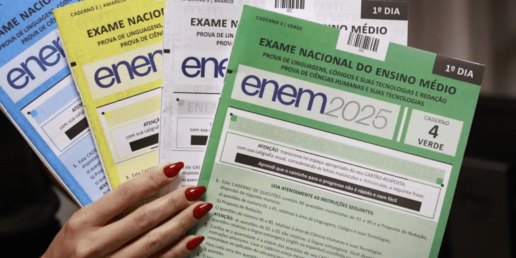 Mão segurando provas do ENEM 2025 com cadernos azul, amarelo, branco e verde.