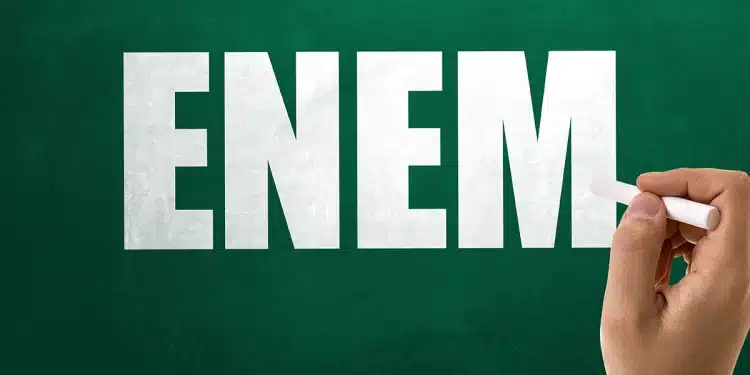 Mão escrevendo a palavra ENEM em um quadro verde, simbolizando debate sobre suspeita de vazamento da prova.