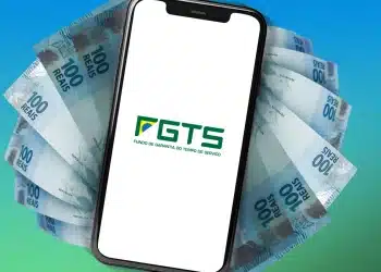 Imagem do logo do FGTS no celular, com cédulas de R$100 ao redor, representando a facilidade de solicitação do saque pelo aplicativo em 2026.
