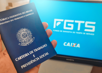 Pessoa segurando celular com o app FGTS da Caixa aberto em frente a notebook exibindo site do FGTS.