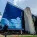 Fachada de um edifício da Previdência Social (INSS) com vidros espelhados refletindo o céu, representando o pagamento de benefícios.