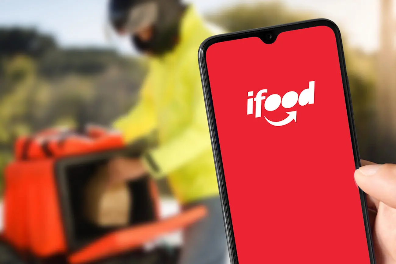 iFood anuncia bônus entre R$ 900 e R$ 3.000 para usuários elegíveis Tela do aplicativo iFood exibida em smartphone enquanto entregador realiza entrega, ilustrando bônus promocional para usuários.