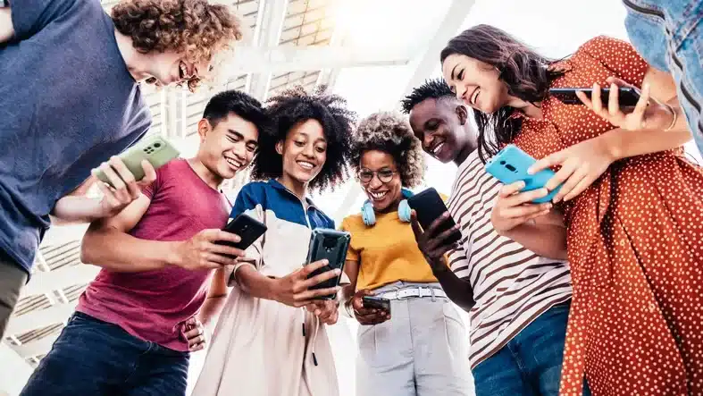 Geração Z. Jovens em círculo, todos curvados e focados individualmente em seus smartphones, ilustrando a imersão digital.