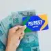 Mão segurando cartão PIS/PASEP da Caixa em frente a notas de 100 reais