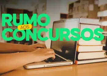 Estudante pesquisando em notebook ao lado de pilha de livros em biblioteca.