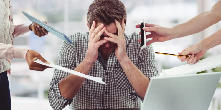 Homem estressado e sobrecarregado no trabalho, com múltiplas tarefas sendo apresentadas ao seu redor, simbolizando o esgotamento profissional (burnout).