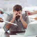 Homem estressado e sobrecarregado no trabalho, com múltiplas tarefas sendo apresentadas ao seu redor, simbolizando o esgotamento profissional (burnout).