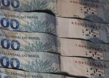 Pessoa segurando notas de 100 reais frente.