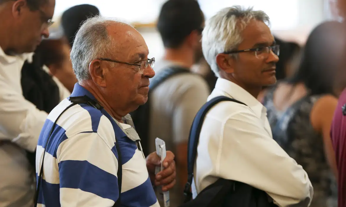 Homens maduros em fila de espera Dois homens maduros com óculos, um de camisa listrada e outro de camisa branca, aguardando em fila