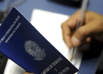 Pessoa segurando carteira de trabalho azul do Brasil enquanto escreve com caneta em papel