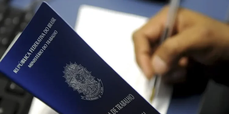 Pessoa segurando carteira de trabalho azul do Brasil enquanto escreve com caneta em papel