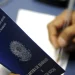 Pessoa segurando carteira de trabalho azul do Brasil enquanto escreve com caneta em papel