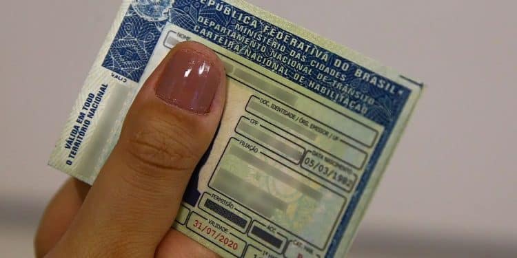 Pessoa segurando a Carteira Nacional de Habilitação (CNH) no formato tradicional. A imagem ilustra o documento que pode ter novas regras de emissão, permitindo a retirada sem a obrigatoriedade de autoescola.