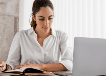 Candidata estudando para concursos públicos com material de preparação e computador em ambiente de estudo.