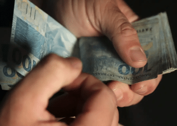 Mãos masculinas contando várias notas de cem reais em ambiente escuro