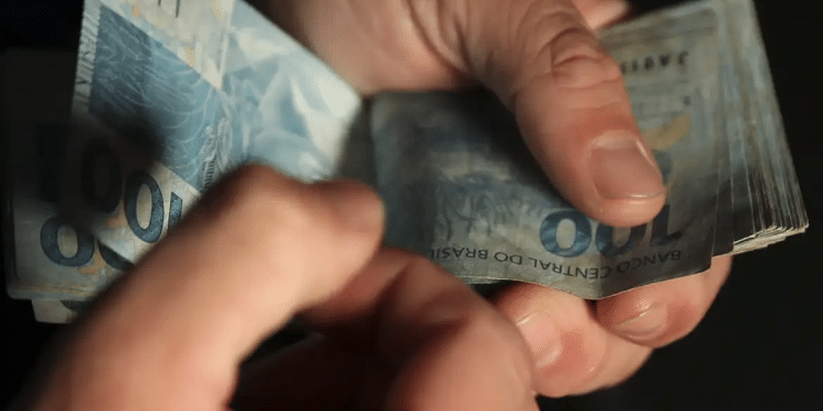 Mãos masculinas contando várias notas de cem reais em ambiente escuro