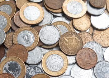 Close-up de diversas moedas antigas de diferentes países e épocas, incluindo peças de cobre e prata, dispostas sobre uma superfície de madeira rústica.