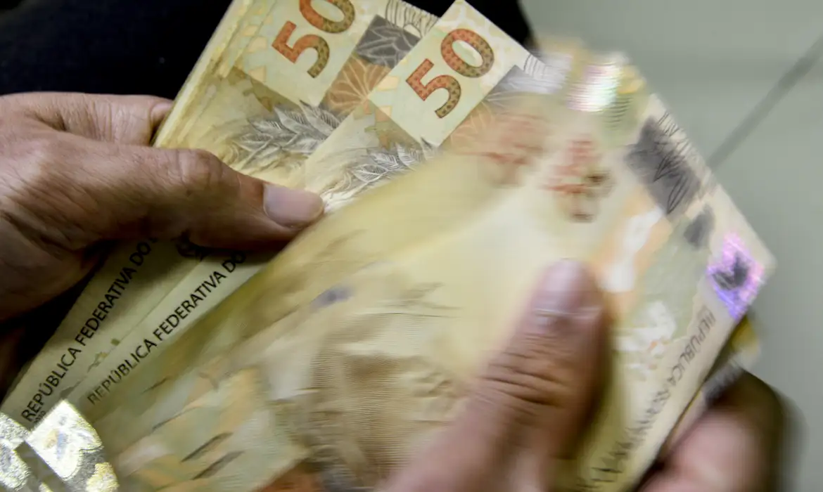 Pessoa contando notas de cinquenta reais Mãos segurando várias cédulas de cinquenta reais brasileiras, contando dinheiro em movimento.