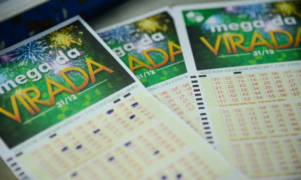 como funciona premio nao acumulativo mega da virada Três volantes da Mega da Virada em primeiro plano, com destaque para as tabelas de números e a marca "31/12", sobre um fundo com cores festivas e fogos de artifício.
