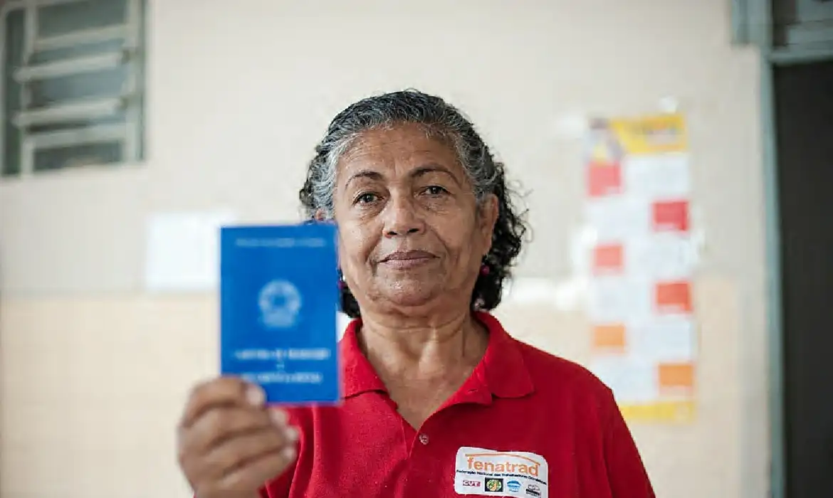 Trabalhadora segurando carteira profissional azul Mulher de meia idade vestindo camiseta vermelha mostrando carteira profissional azul em foco