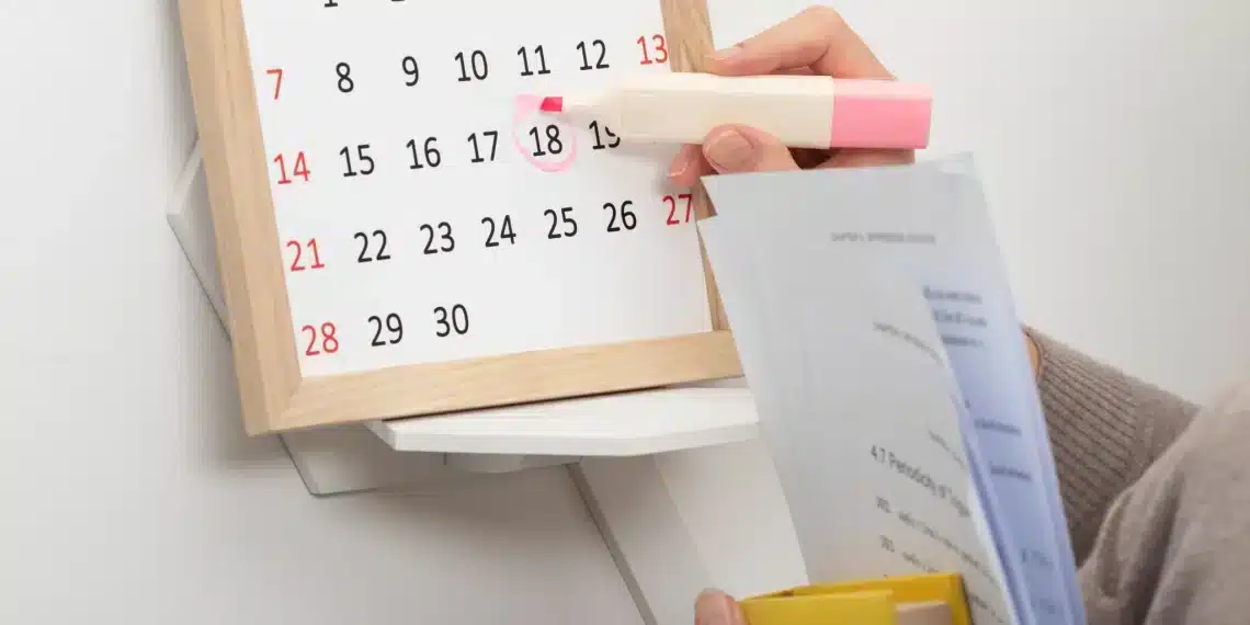 Marcar Data Importante no Calendário com Marca-Texto Rosa Mão segurando marca-texto rosa circulando dia 18 em calendário de mesa com moldura de madeira