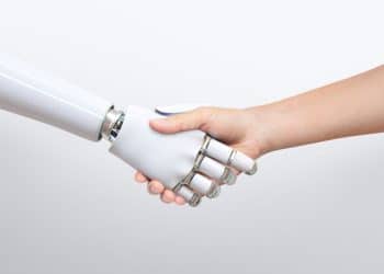 Aperto de mão entre uma mão humana e um braço robótico branco, simbolizando a parceria entre humanos e Inteligência Artificial (IA) no mercado de trabalho e as profissões impulsionadas pela tecnologia.