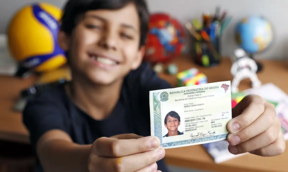 Pré-requisitos 2ª Via RG Menor 16 Anos Documentação Criança segurando o documento de identidade (RG). A imagem representa a emissão da segunda via para menores de 16 anos, que precisam da presença do responsável legal.