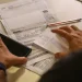 Pessoa organizando contas e segurando smartphone sobre mesa com papéis e caneta