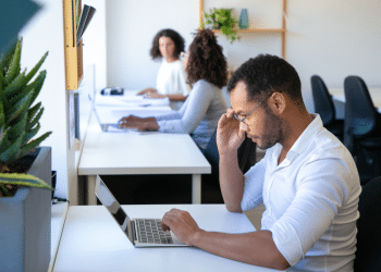 Jovens profissionais diversos trabalhando concentrados em laptops em escritório com decoração moderna e plantas