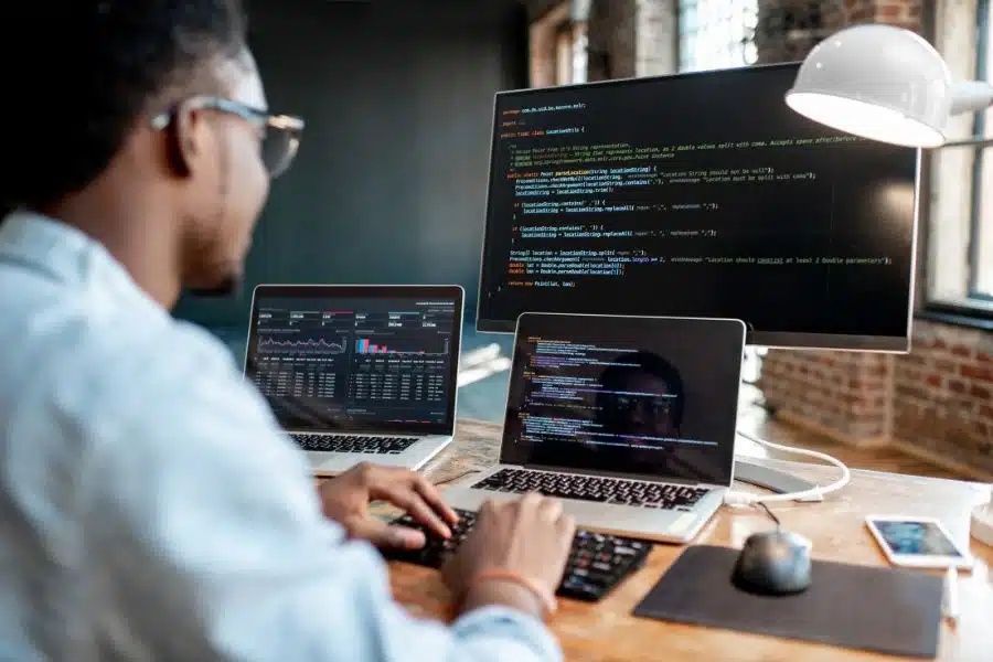 Analista trabalhando com automação e dados. Profissional analisando dados e programando em múltiplas telas em ambiente de trabalho tecnológico.