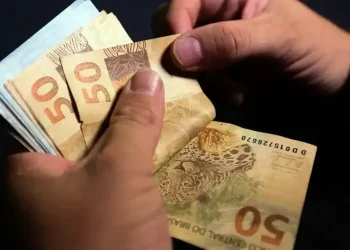 Mãos manuseando cédulas de cinquenta reais simbolizando o valor de R$ 1.050 do benefício Pé-de-Meia.