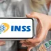 Pessoa segurando um celular com o logo do INSS e cédulas de dinheiro, simbolizando o pagamento do 13º salário do INSS.