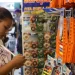 Mulher analisando produtos escolares em prateleira com fitas coloridas e réguas laranja à venda