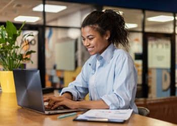 Jovem sorridente digitando em notebook durante curso de qualificação profissional gratuito