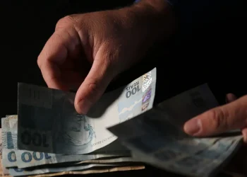 Mãos manuseando cédulas de real representando o benefício financeiro do Pé-de-Meia Licenciaturas.