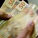 Notas de cinquenta reais sendo contadas, representando o benefício financeiro do novo programa do governo.
